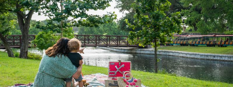 A mom and child have a picnic by the water at Landa Park.