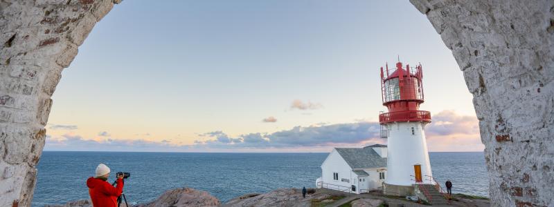 Kvinne i orange jakke fotograferer Lindesnes Fyr