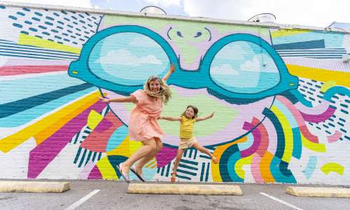 Mother and daughter jumping in front of a mural