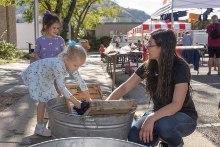 Two children learn to wash clothes in buckets outdoors with an adult at Golden History Museum & Park Autumn Fest
