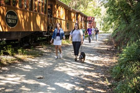 two people walking on rail trail with their dog next to northern central railway of york's steam engine