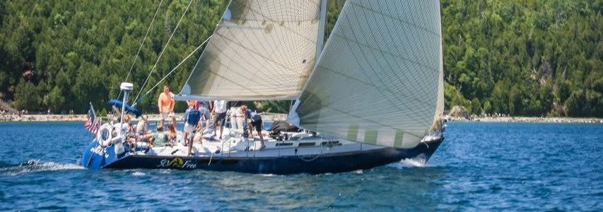 A sailboat cruises through calm blue waters off the forested shore of Michigan’s Mackinac Island