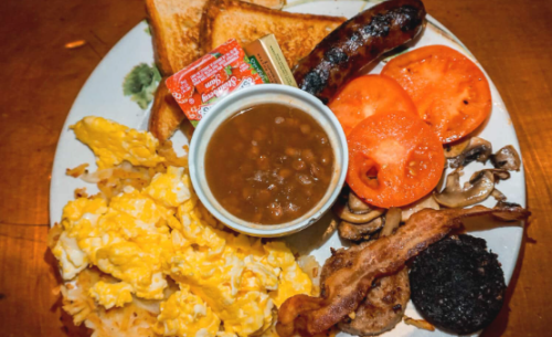Platter of scrambled eggs, bacon, sausage, roast, potatoes, and jam