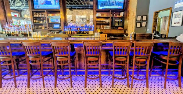Tall wooden chairs face a shiny bar with a variety of liquor bottles on the shelves