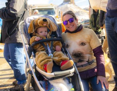 A baby dressed in a Golden retriever costume and parent with a golden retriever shirt at the 2022 Goldens in Golden event