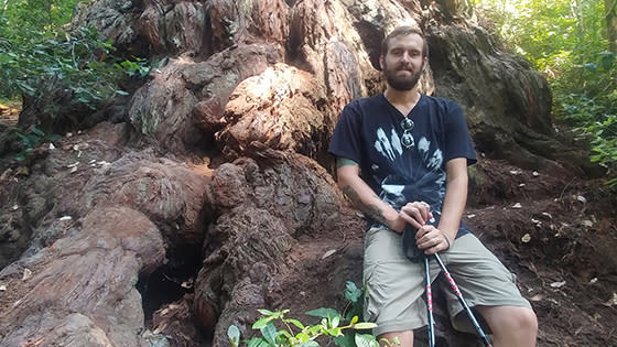 Austin posing while hiking in front of  the largest known redwood in the world, Hyperion, in Redwood National Park.