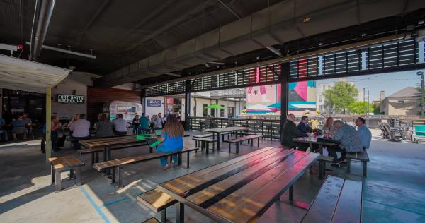 A shot of the lively bakery district patio, guests are chatting over a meal.