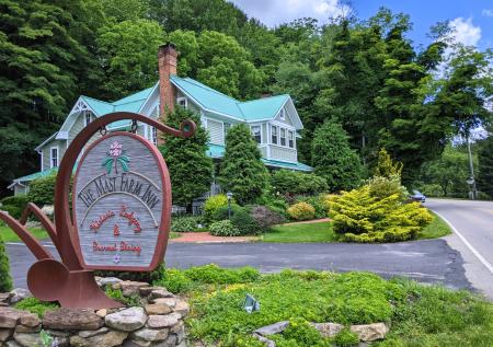 A sign reading "The Mast Farm Inn Historic Lodging & Gourmet Dining" is seen in front of a large house with a green roof.