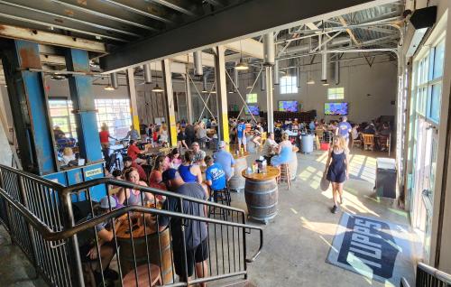 Large room with people, beer barrels, tables, and metal fixtures