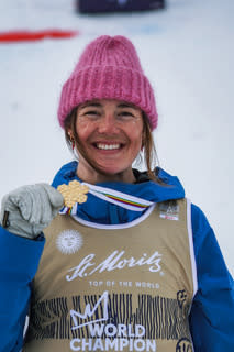 Smiling womaan in pink beanie and ski gear holding out a gold medal around her neck