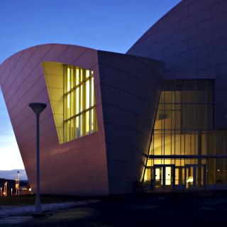 An irregular shaped building at sunset with lighted glass front
