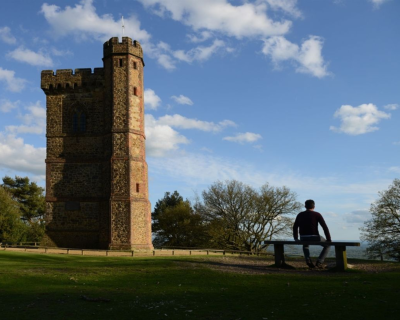 A man sits on a bench next to Leith Tower enjoying the view across from the top of Leith Hill