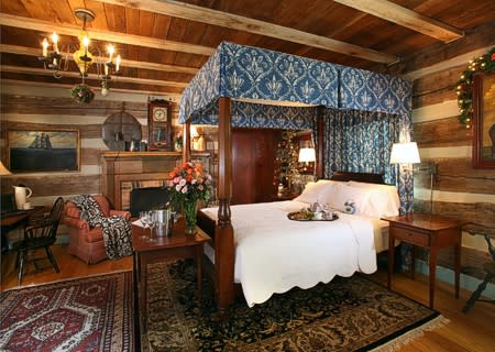 Four poster bed with blue hangings, white cover and oriental rugs on the hardwood floor.