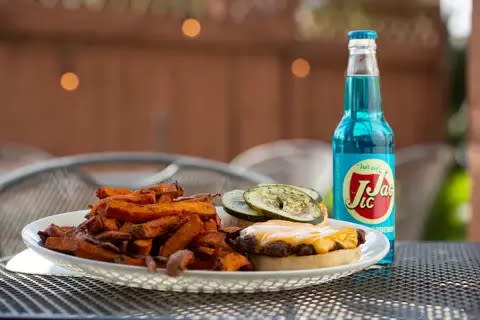 A burger is served with a blue soda and side of sweet potato fries at Fizz Burgers and Bottles.
