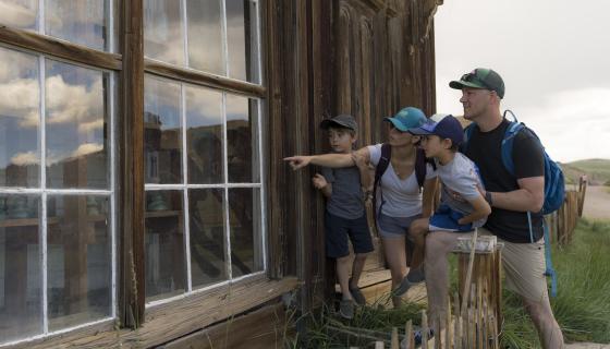 Family looking inside a window of an old building at bodie state historic park