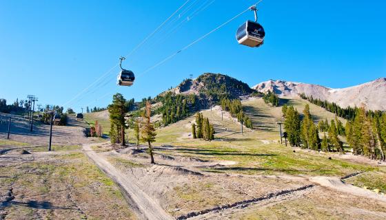 Mammoth Mountain scenic gondola cars hanging over grass and dirt with peaks in the background
