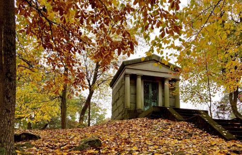A crypt at the Sleepy Hollow Cemetery surrounded by autumn leaves in orange and yellow.