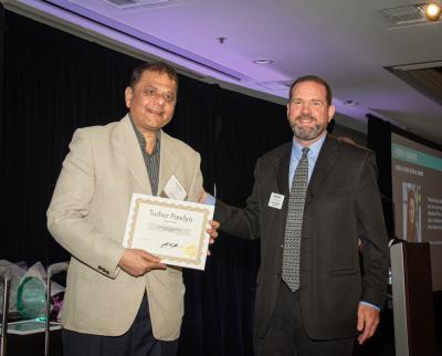 Tushar Pandya holding certificate for the Unsung Hero Award next to Trevor Bridge, Chair of Board of Directors