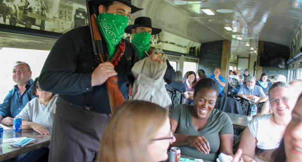 in a train full of people, two men dressed up as desperados pretend to rob a smiling group of people