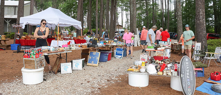 A woman browses a table full of antiques, including collectible signs, surrounded by trees at the Tobacco Farm Life Museum during the 301 Endless Yard Sale.