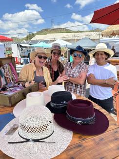Golden Hayride & Outpost Hat Craft activity showcasing a handful of western style hats decorated and also being worn by four people with the Outpost farmers market in the background.