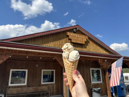 a hand holds a waffle cone of ice cream in front of the exterior view of Cassville Country store