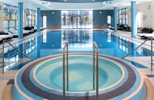 An empty and tranquil clear blue pool with a round jacuzzi pool in the forefront