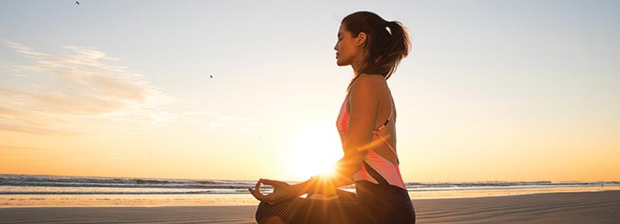 A woman sits in a yogic lotus position on Daytona Beach at sunrise.