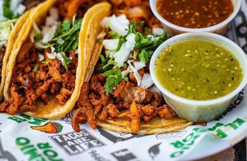 Plate of al pastor tacos with green and red salsa