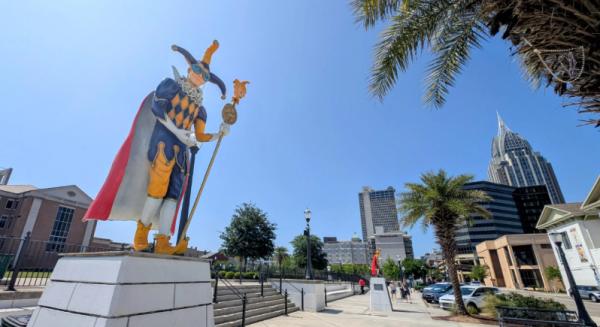 A painted statue of a jester stands tall with brick buildings behind it