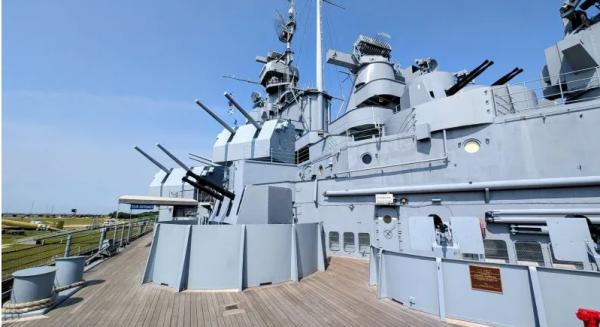 The deck of a large battleship painted gray with wooden floors.