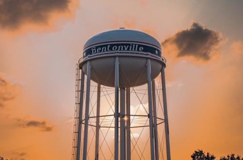 A Bentonville branded water tower with a bright orange sunset behind it.