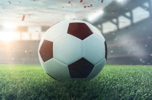 A soccer ball rests on the grass of a stadium.