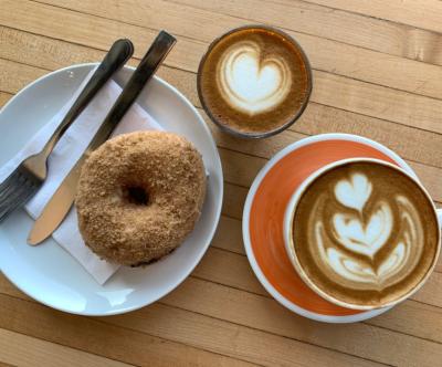 View from above of donut on plate next to two cups of coffee topped with artful foam designs at Roosevelt Coffeehouse