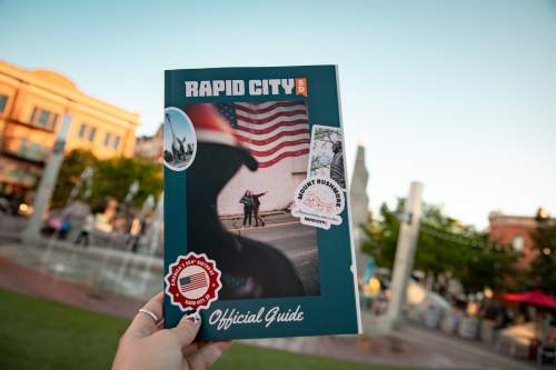 The cover of the Visit Rapid City guide is held up by a woman against the backdrop of the fountains at Main Street Square.
