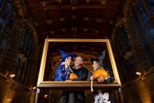Children and a grandparent standing inside a giant gold picture frame dressed in Halloween costume beneath a high ceiling of the Guildhall