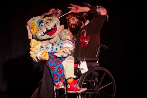 A performer in the a wheelchair holds a puppet at the Fringe Arts Festival