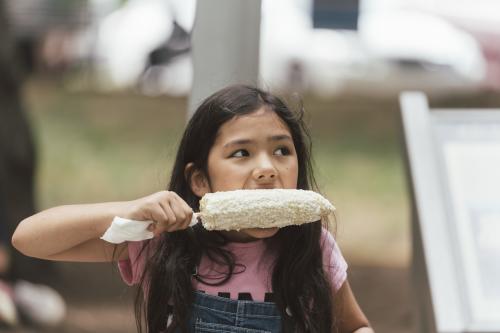 Young girl eating Mexican street corn at Hola Asheville Festival