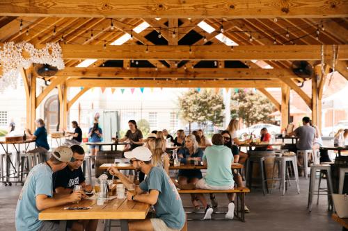 People sit at outdoor picnic tables on a covered patio.