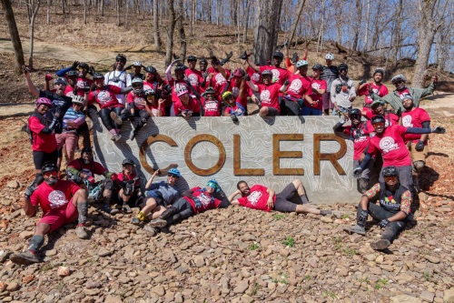 A group of people in red t-shirts posing in front of a sign that reads Coler