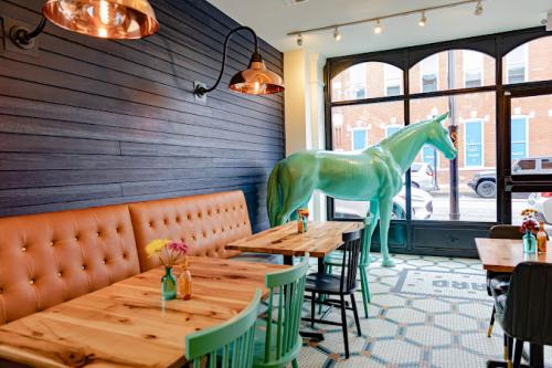 Dining room at Bentonville Taco and Tamale, featuring unique tiled floor, brown leather banquette seating, and the signature big blue plastic horse gazing out the window.