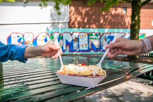 Two hands holding plastic spoons in the Hartzell's banana split