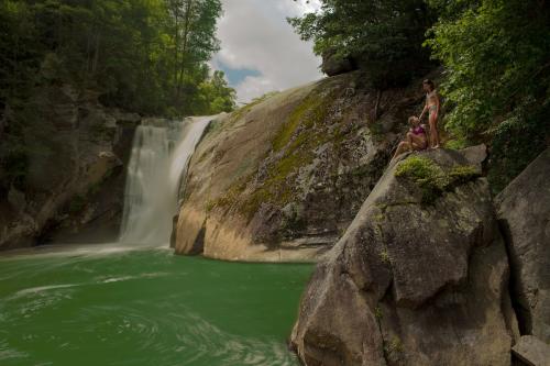 Two children are on a large boulder to the right of a large pool with a waterfall flowing into it.