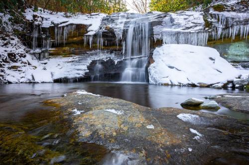 A waterfall with a shallow pool at the bottom is dusted in a light layer of snow.