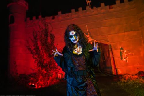 A woman dressed as a zombie with a white face and blood streaking down it poses with her hands raised in front of a castle at Frightland amusement park in Middletown, Delaware.