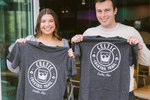 A couple holding up their Celtic Cocktail Trail t-shirt after completing the trail