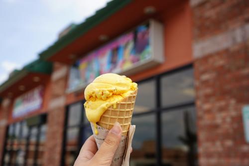 A close up photo displays a double scoop of mango ice cream in a waffle cone in front of Delicias Michoacanas in Fort Smith, Arkansas.
