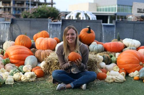 Woman holding a pumpkin in front of a fountain.