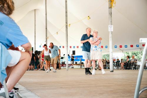 Two couples dancing at Pulaski Polka Days in a large tent on the dance floor and others watching.