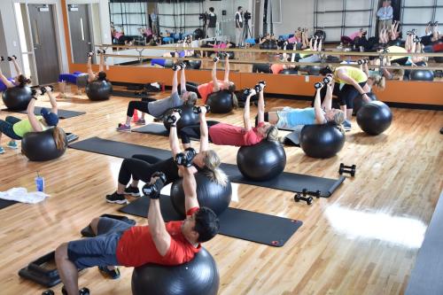 Group exercise class at a fitness center with people lifting weights over their heads